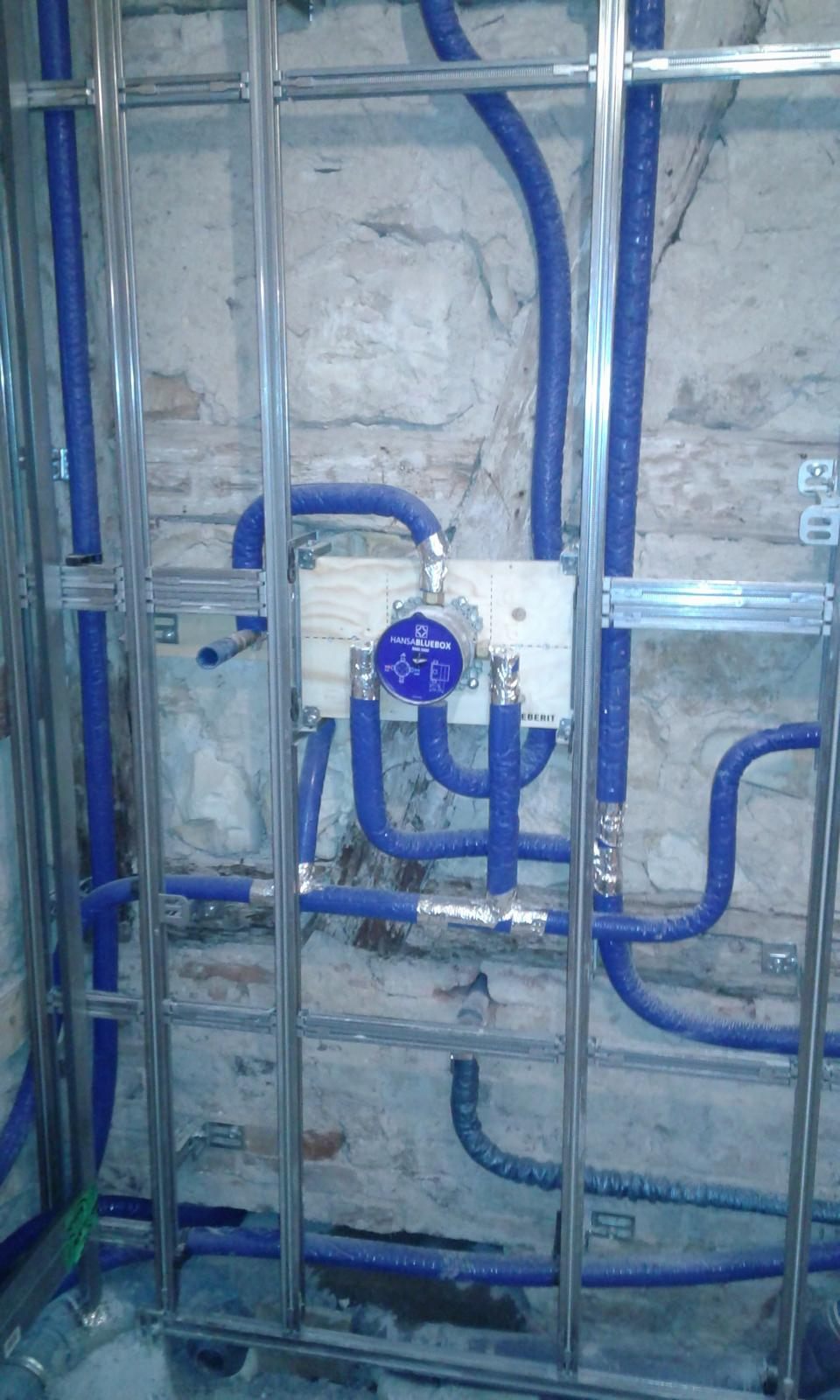 Sanitärinstallation im Rohbau mit gedämmten Leitungen vor altem Bruchsteinmauerwerk